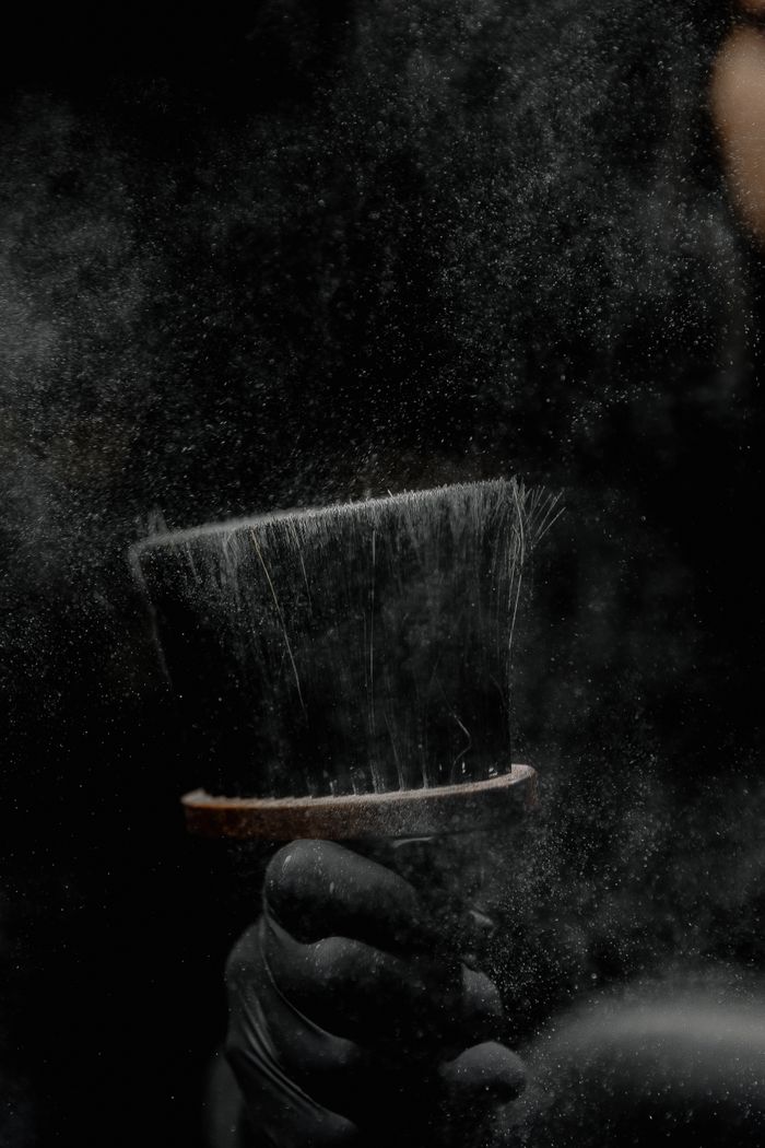 A detailed view of a barber's brush with dust particles against a dark background.